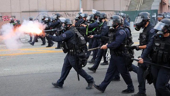 A police officer uses stun grenades during clashes with protesters outside the Los Angeles Federal Building.