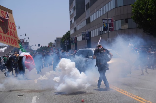 A cloud of tear gas envelops a street as protesters face a line of law enforcement in downtown Los Angeles.